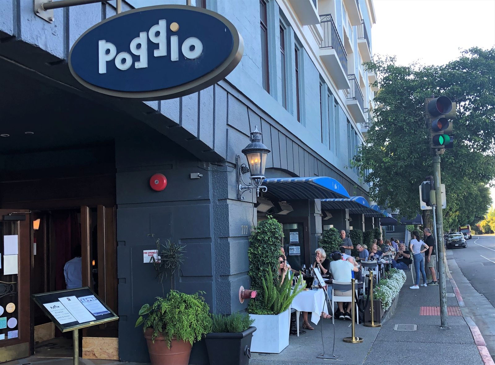 Poggio entrance with its oval blue sign and outdoor tables along a sidewalk