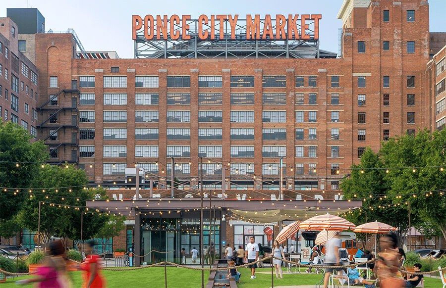 The large red brick Ponce City Market building with its rooftop sign above a lawn with umbrellas