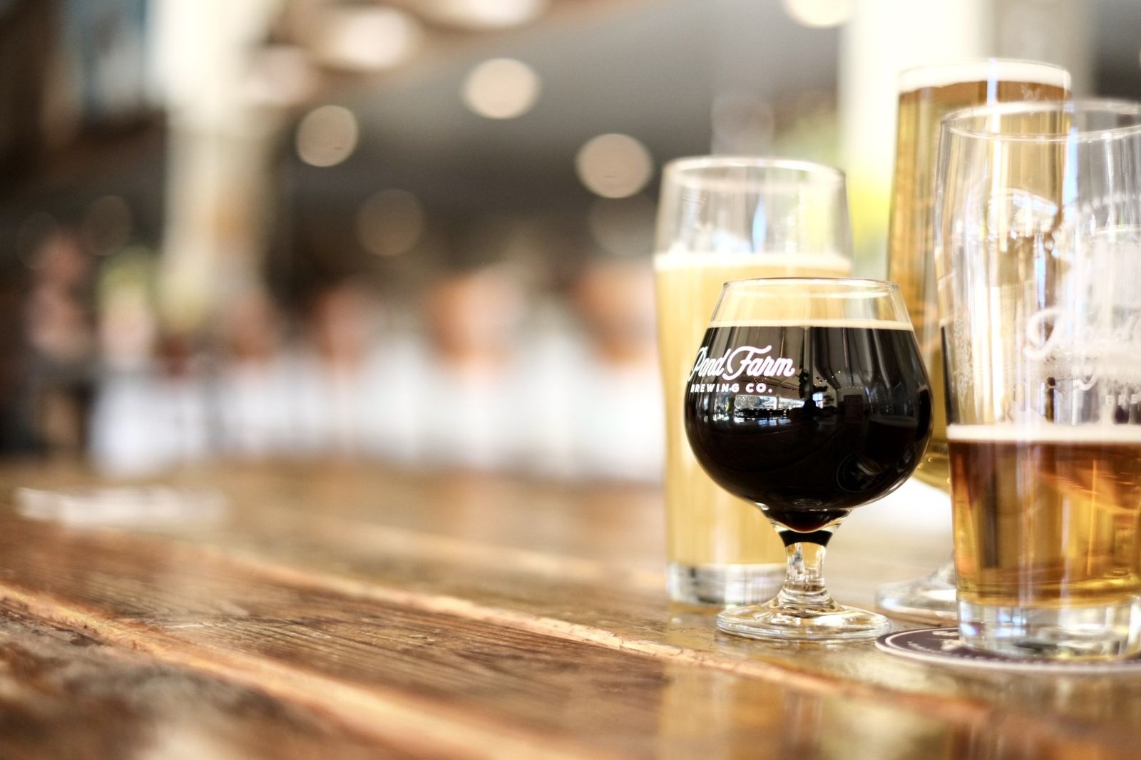 Flight of beer glasses on a wooden bar with a blurred taproom behind