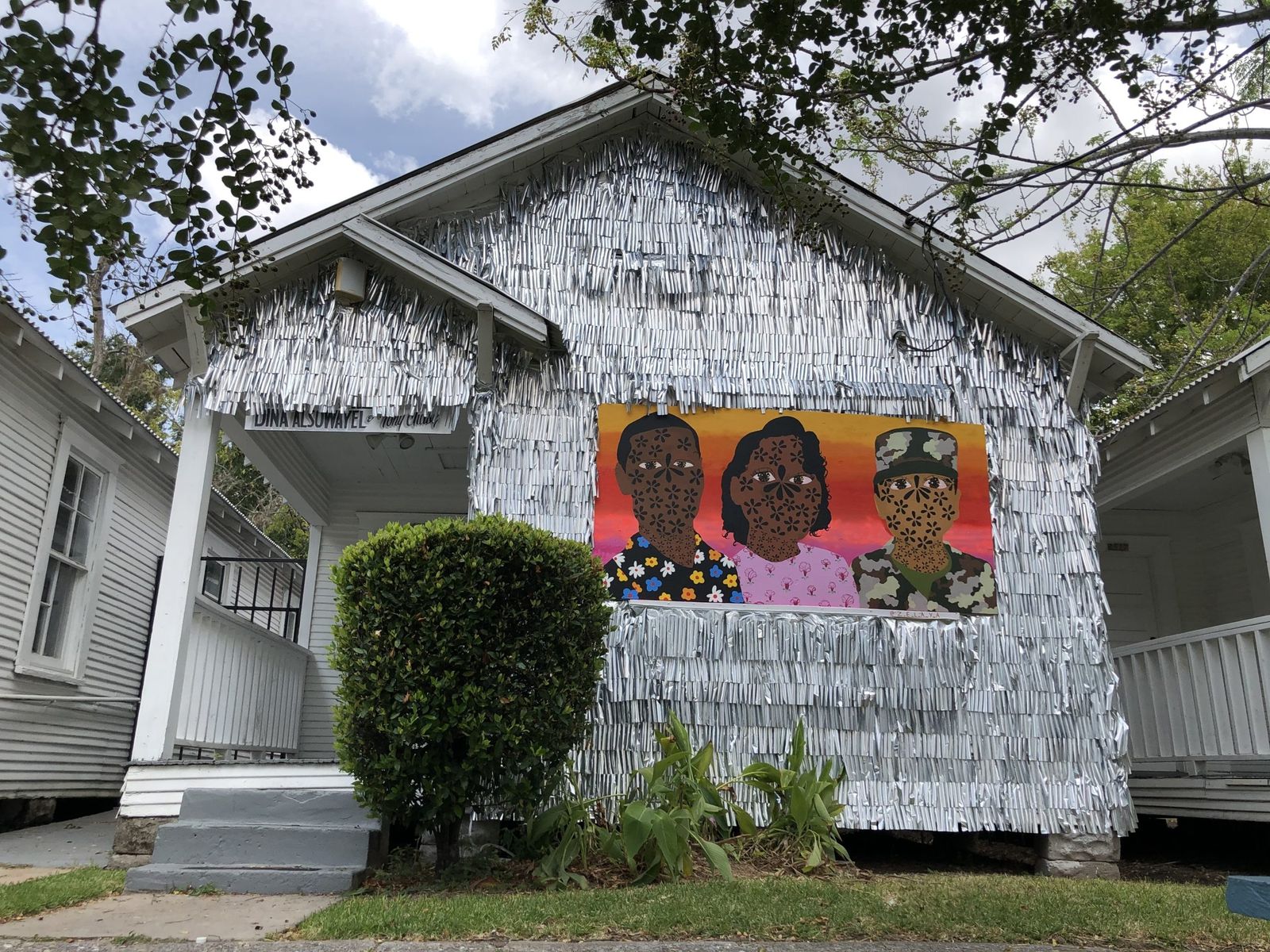 A shotgun-style row house covered in silver tags with a painted mural of three portraits on its front