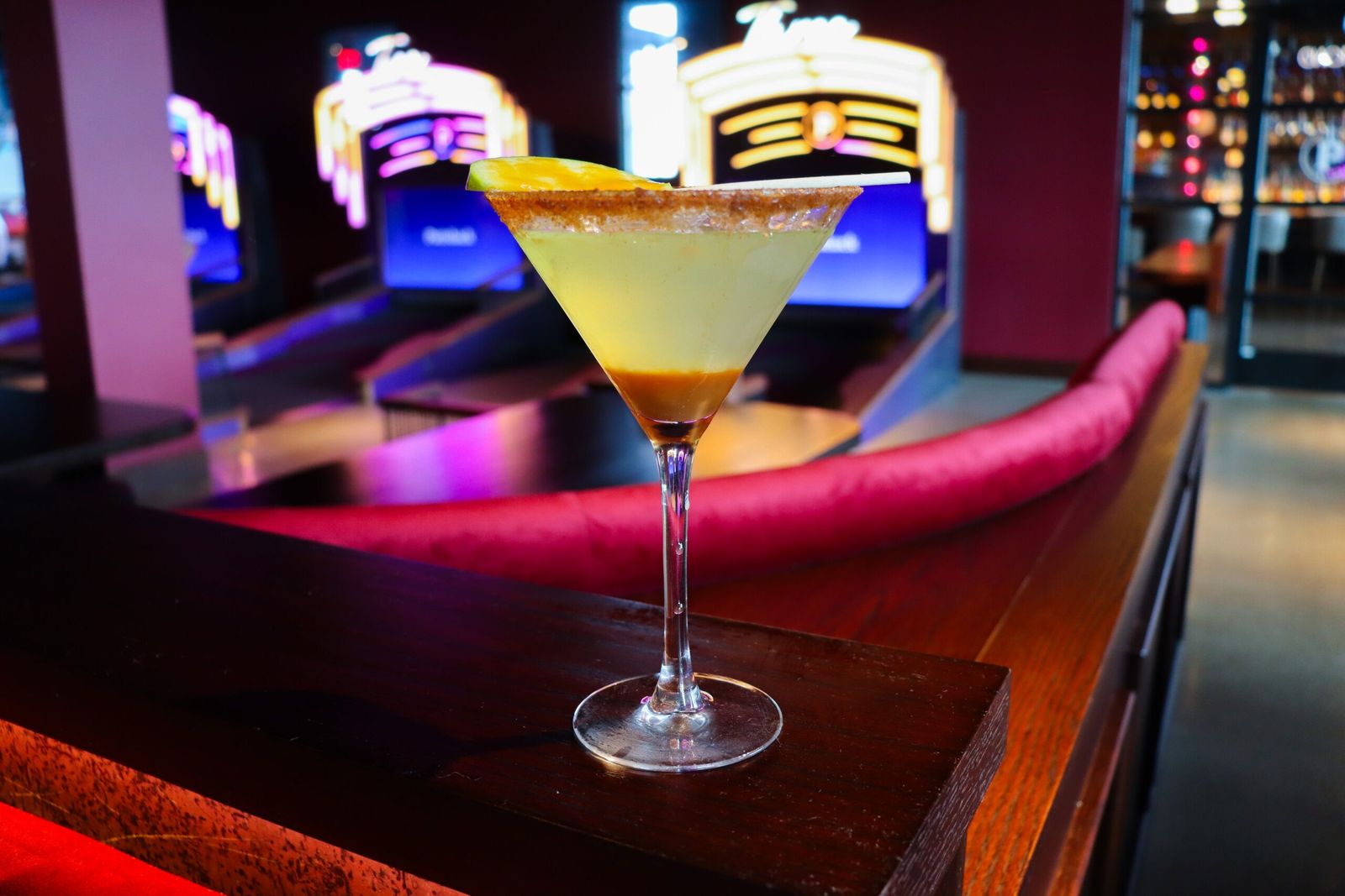 A lemon-rimmed martini on a lounge table with lit mini golf holes in the background