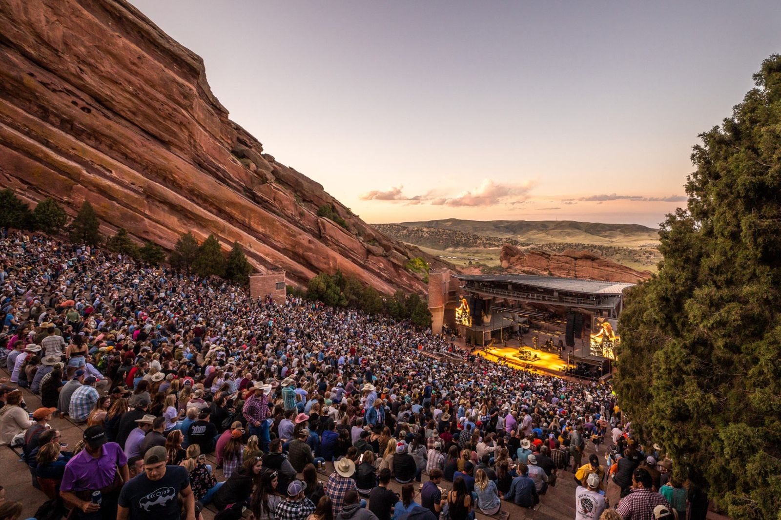 A packed amphitheater of seated spectators between tall red sandstone rocks at sunset.