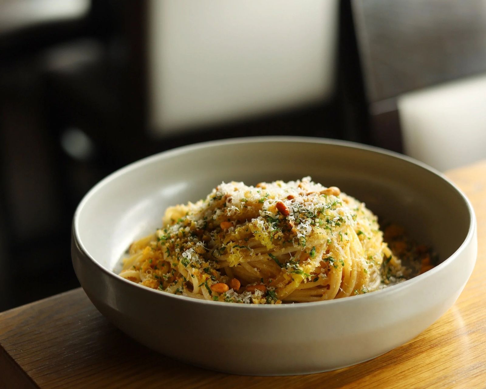 A shallow bowl of pasta with herbs and breadcrumbs on a wooden table.