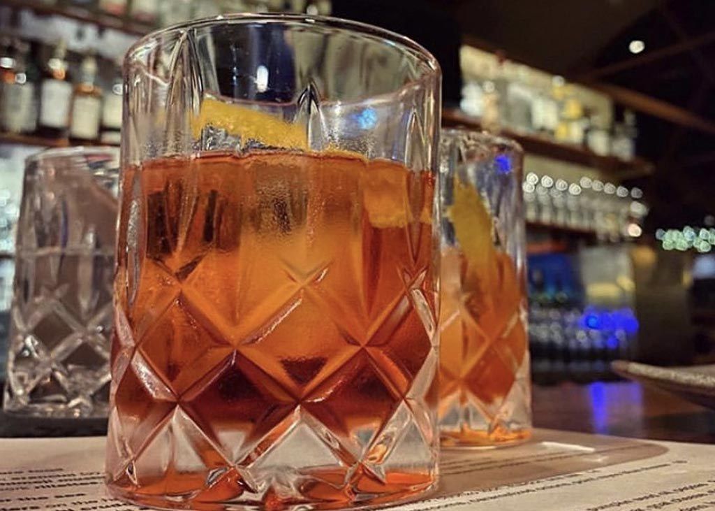 Two cut-crystal glasses of an orange cocktail on a bar