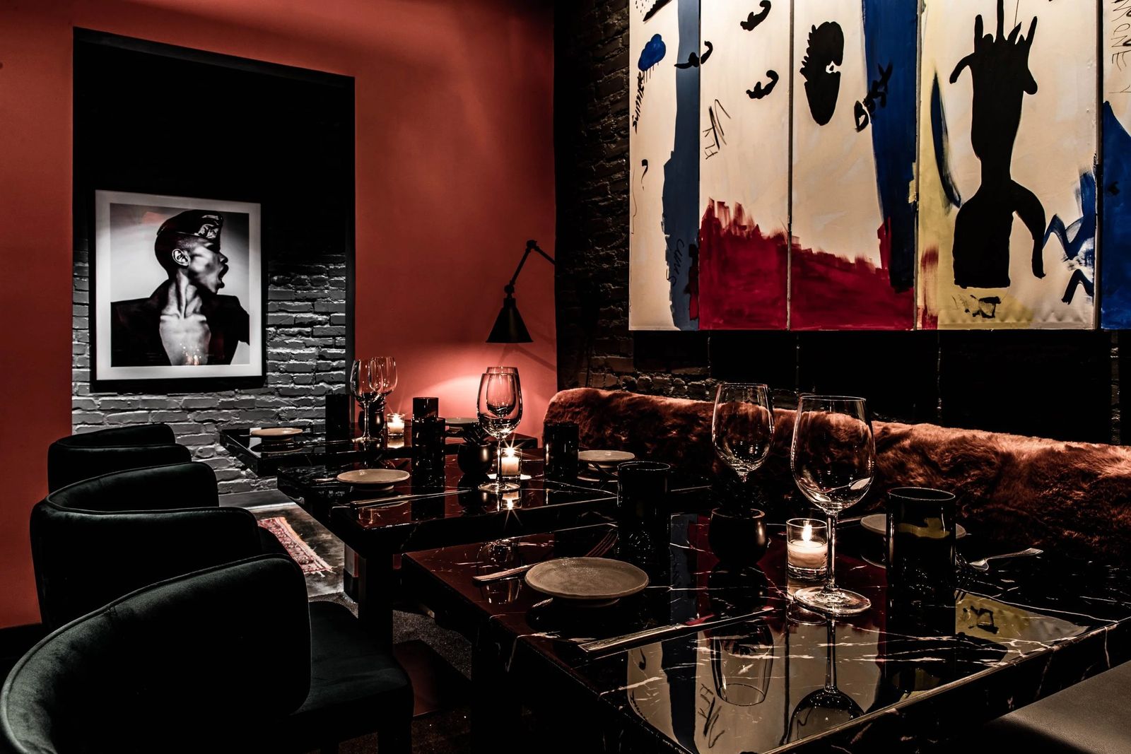 Dimly lit dining room with a banquette, candlelit tables and framed art on the walls