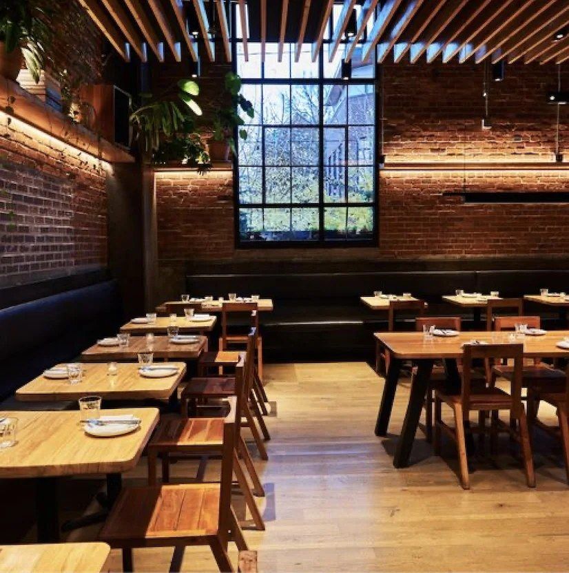 Empty restaurant dining room with wooden tables, brick walls and a large window