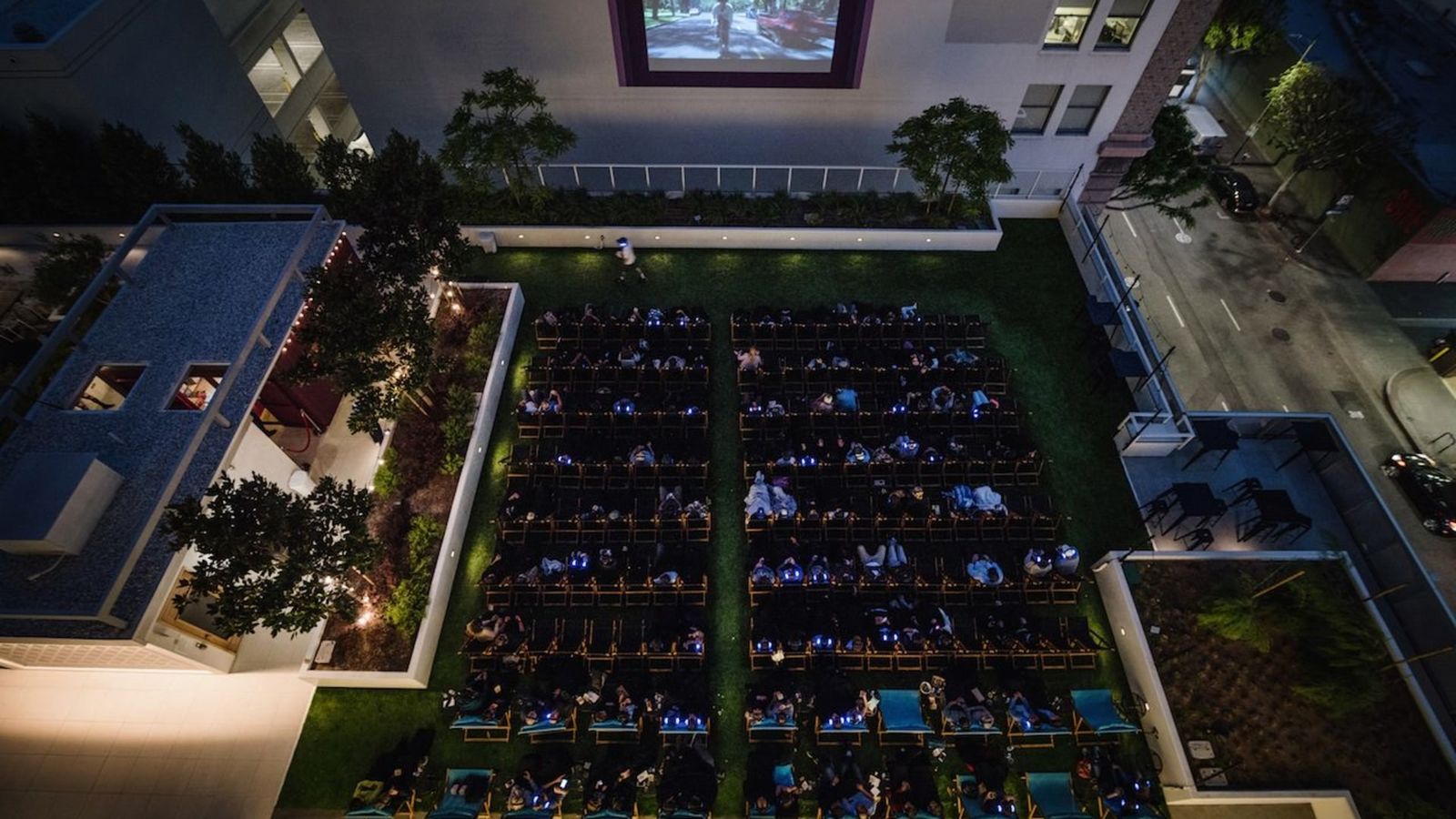 Aerial night view of a rooftop cinema with rows of seats facing a large screen