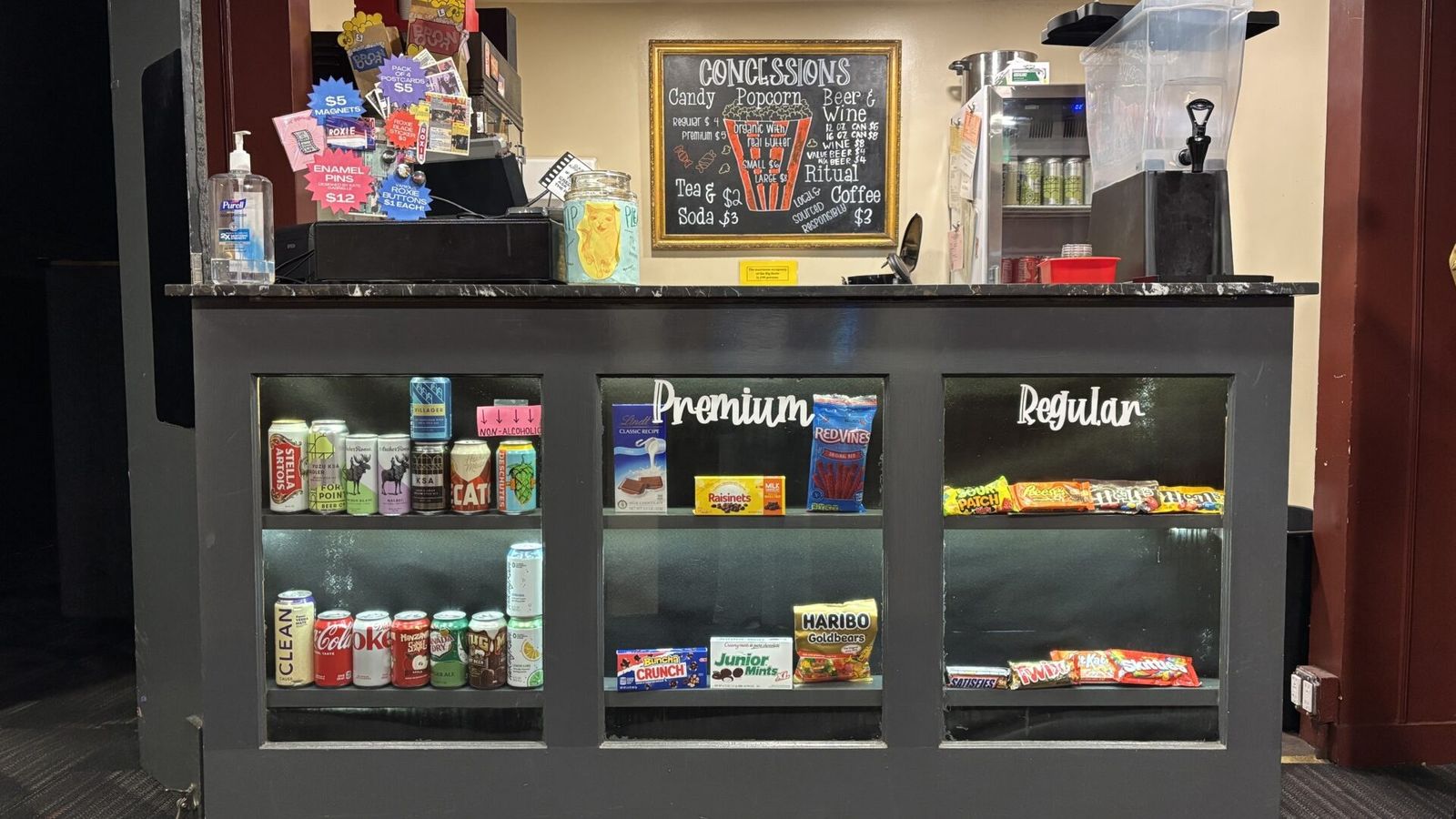 A theater concession counter with shelves of snacks and drinks and a chalkboard menu.