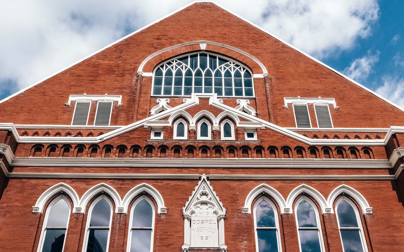 Red brick gabled facade of the Ryman Auditorium with arched windows under a blue sky