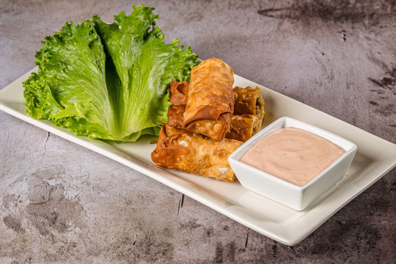 A plate of fried appetizer rolls with a dipping sauce and lettuce