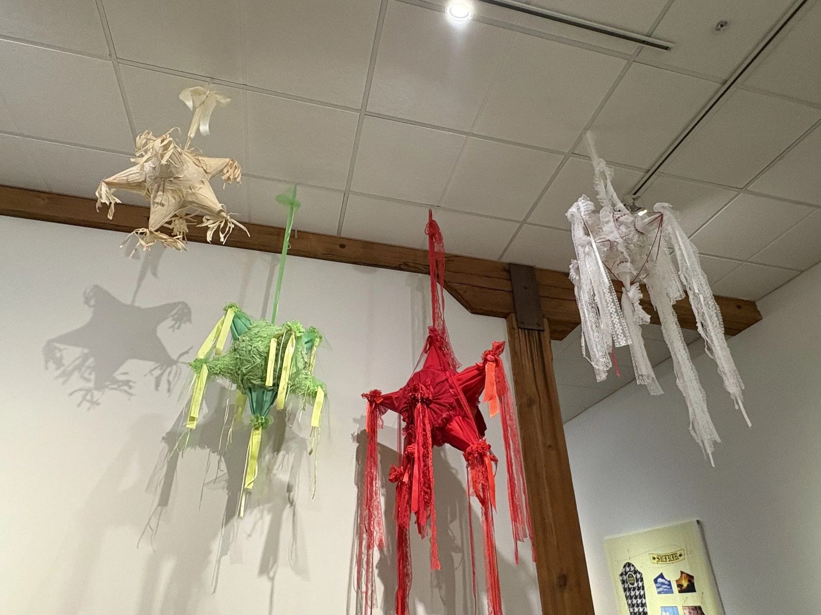 Sculptural paper and fabric figures hanging from the ceiling of a white gallery room