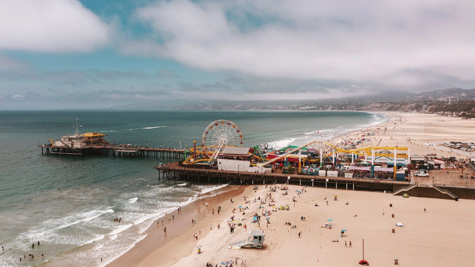 An aerial view of the pier with its Ferris wheel and the beach and shoreline beside it.