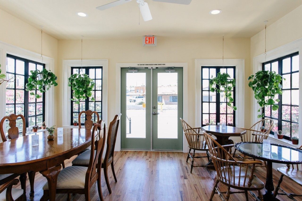 Bright dining room with wooden tables and chairs, tall windows and a glass-paned double door