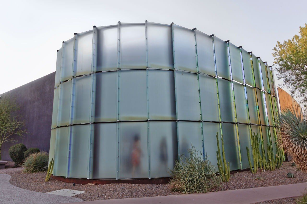 Curved frosted-glass cylinder of the museum building surrounded by desert plants