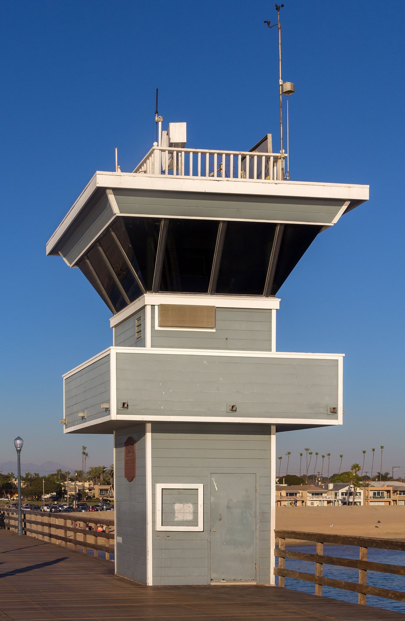 A gray lifeguard and harbor tower on a wooden pier under a blue sky.