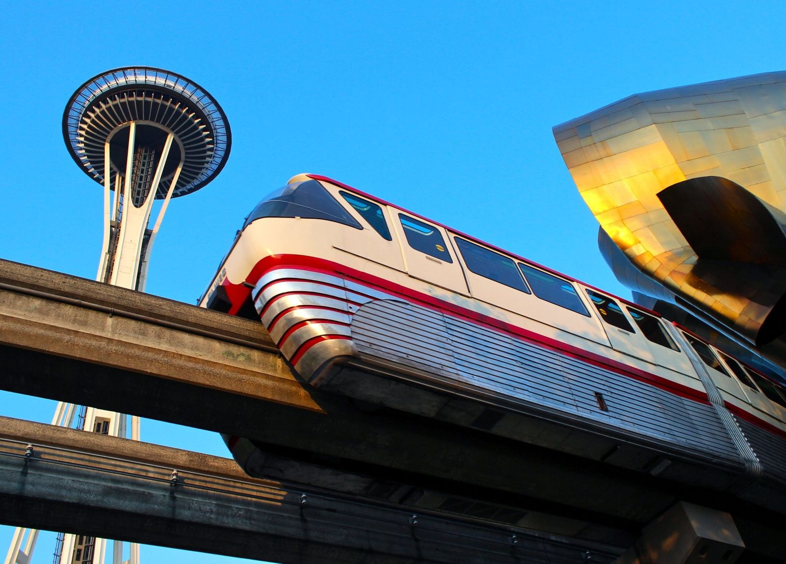 A monorail train on its elevated track beside the Space Needle against a blue sky.