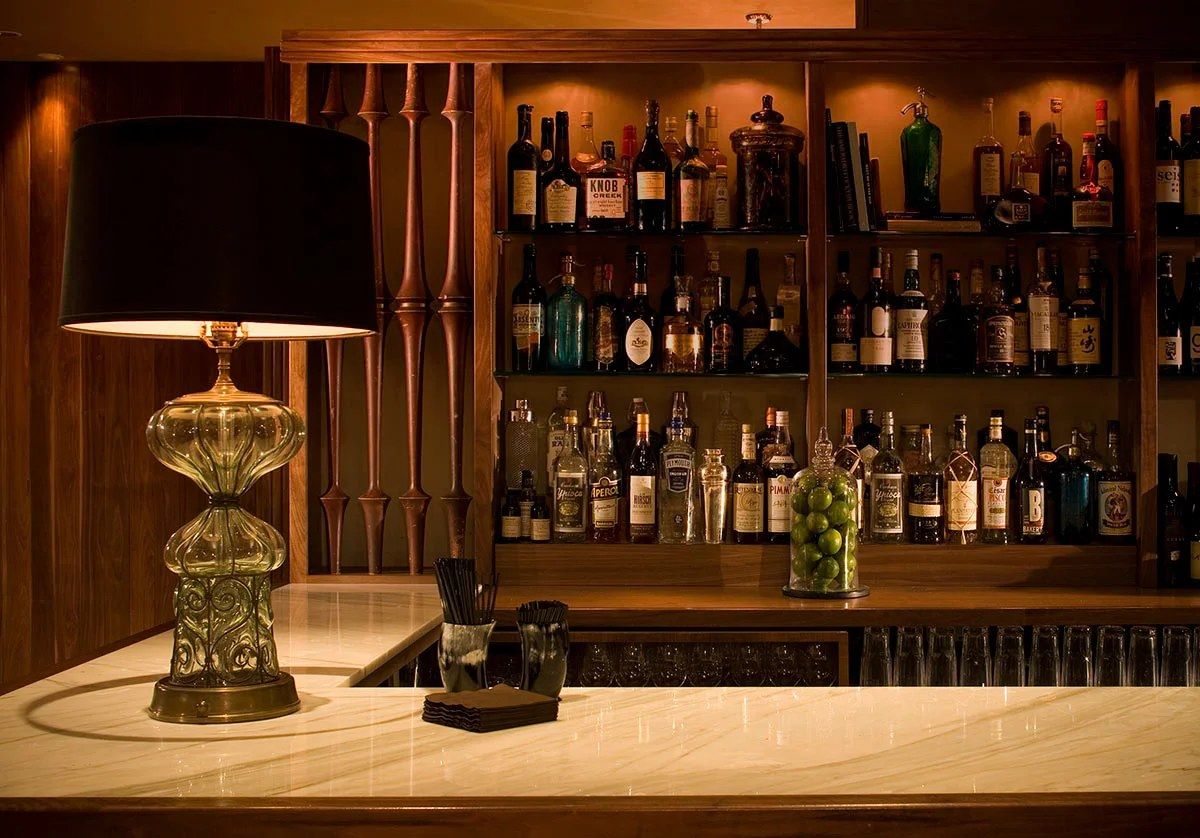 A marble bar counter with a glass lamp and shelves of bottles behind it.