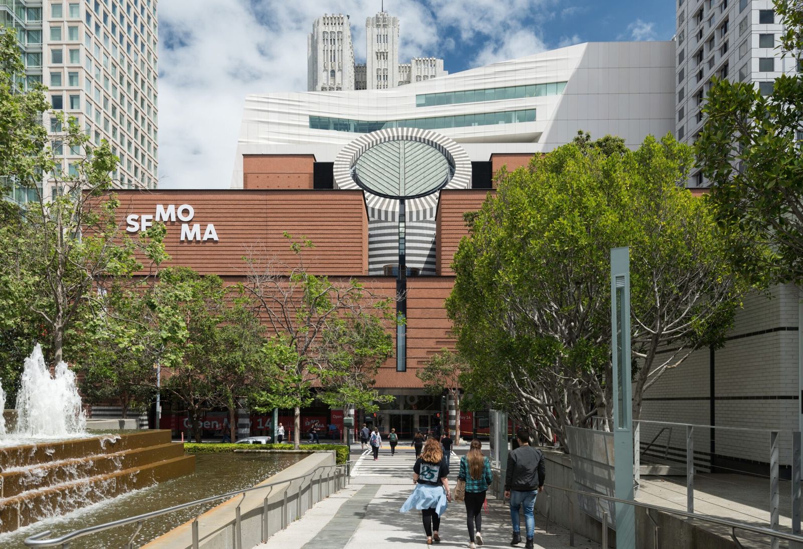 The museum's brick facade and a round skylight tower above a fountain plaza with trees.