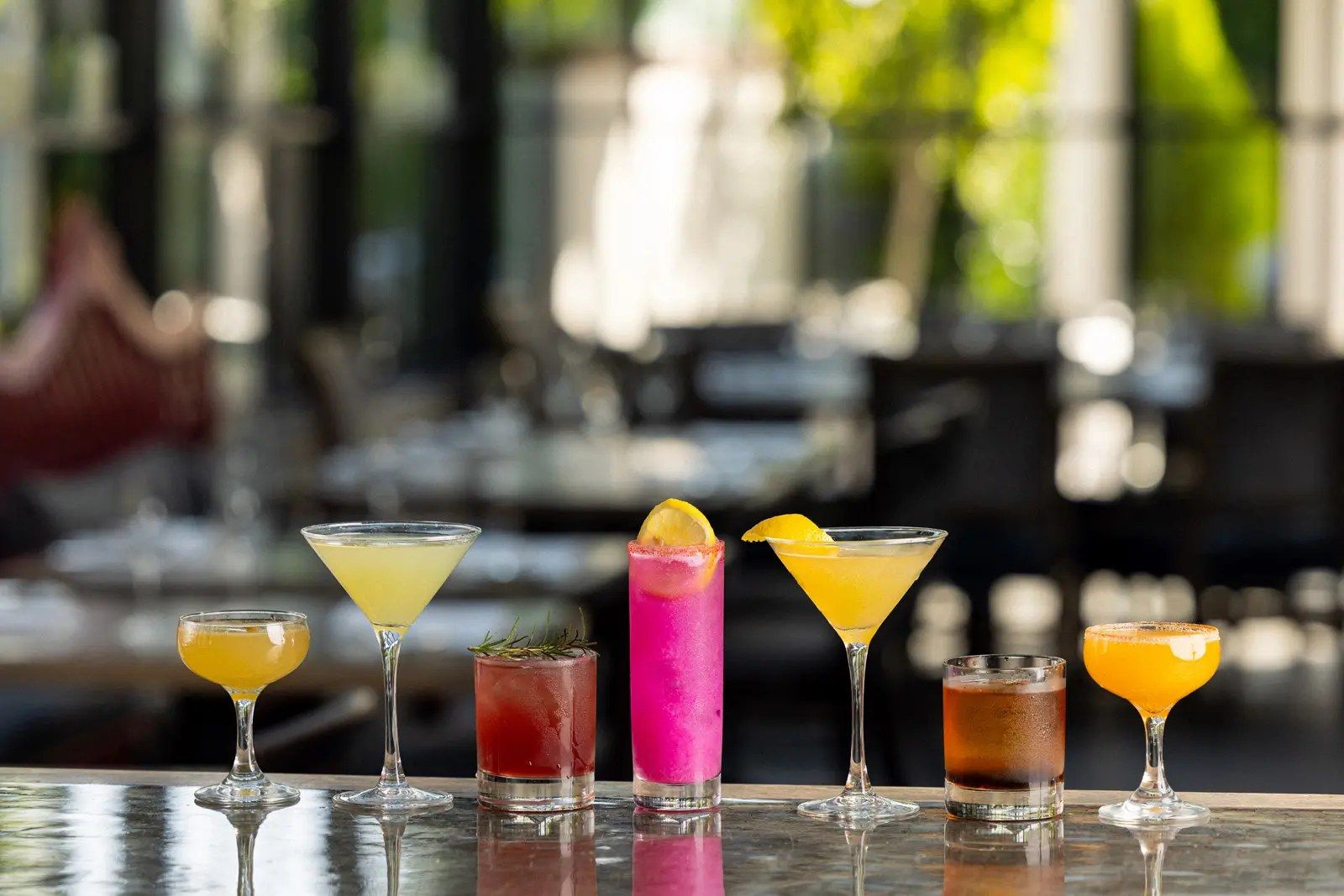 A row of colorful cocktails on a bar counter in a restaurant.