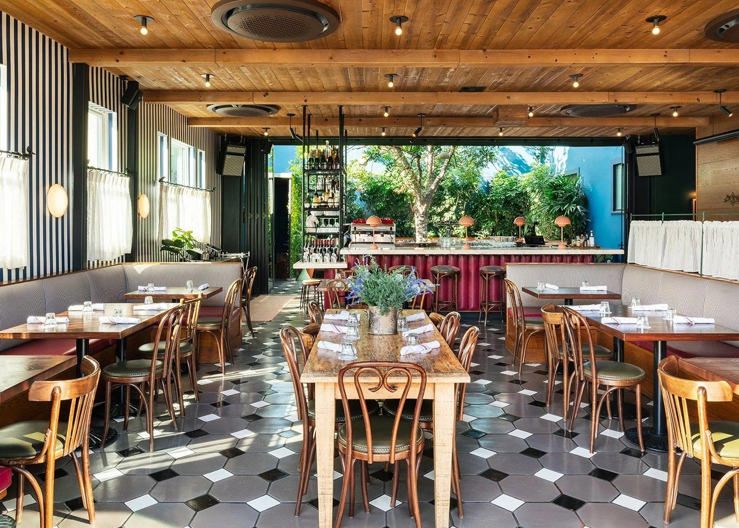 Dining room with wooden tables, bentwood chairs, banquettes and a black and white checkered floor