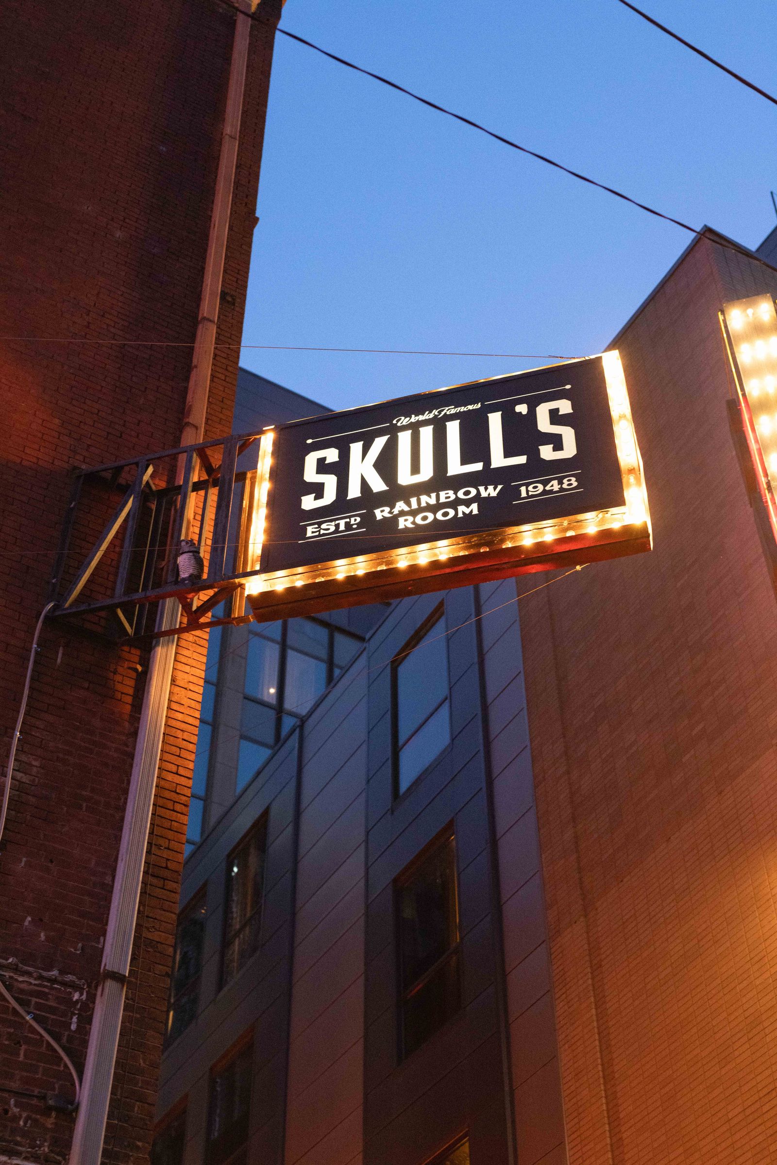 Lit Skull's Rainbow Room sign on a brick building at dusk