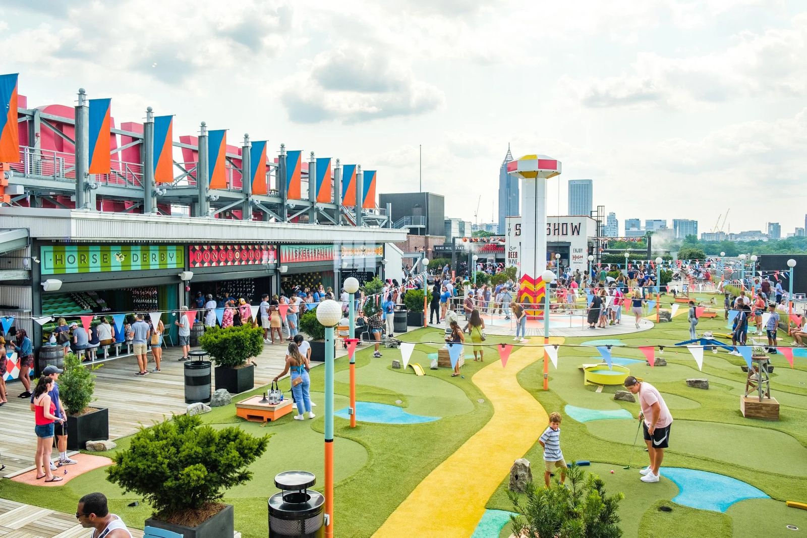 A rooftop mini golf course with a winding yellow path, colorful banners and the city skyline in the distance