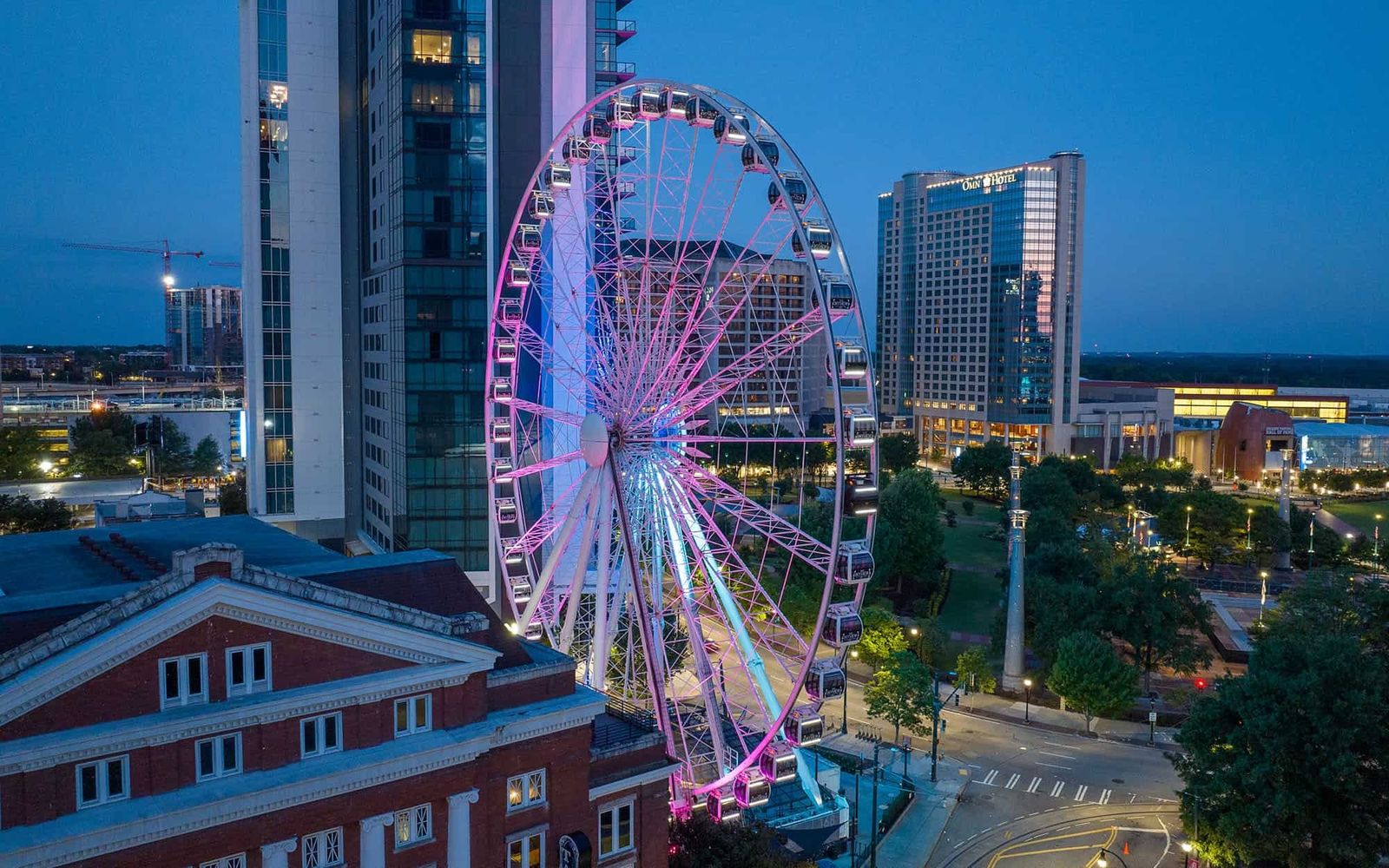 The SkyView Ferris wheel lit in pink and blue at dusk beside downtown towers