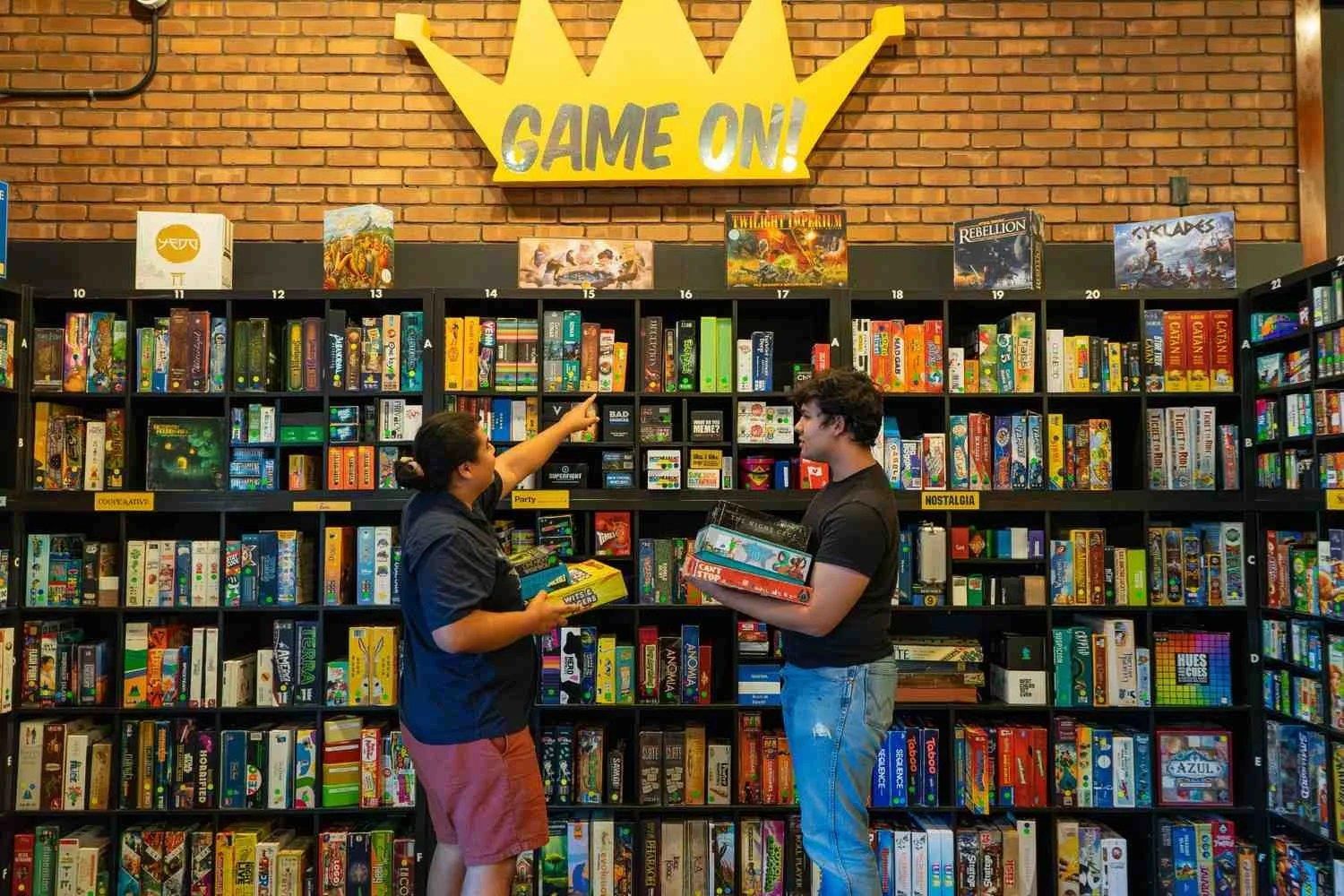 Shelves packed with board games with two people browsing under a Game On sign