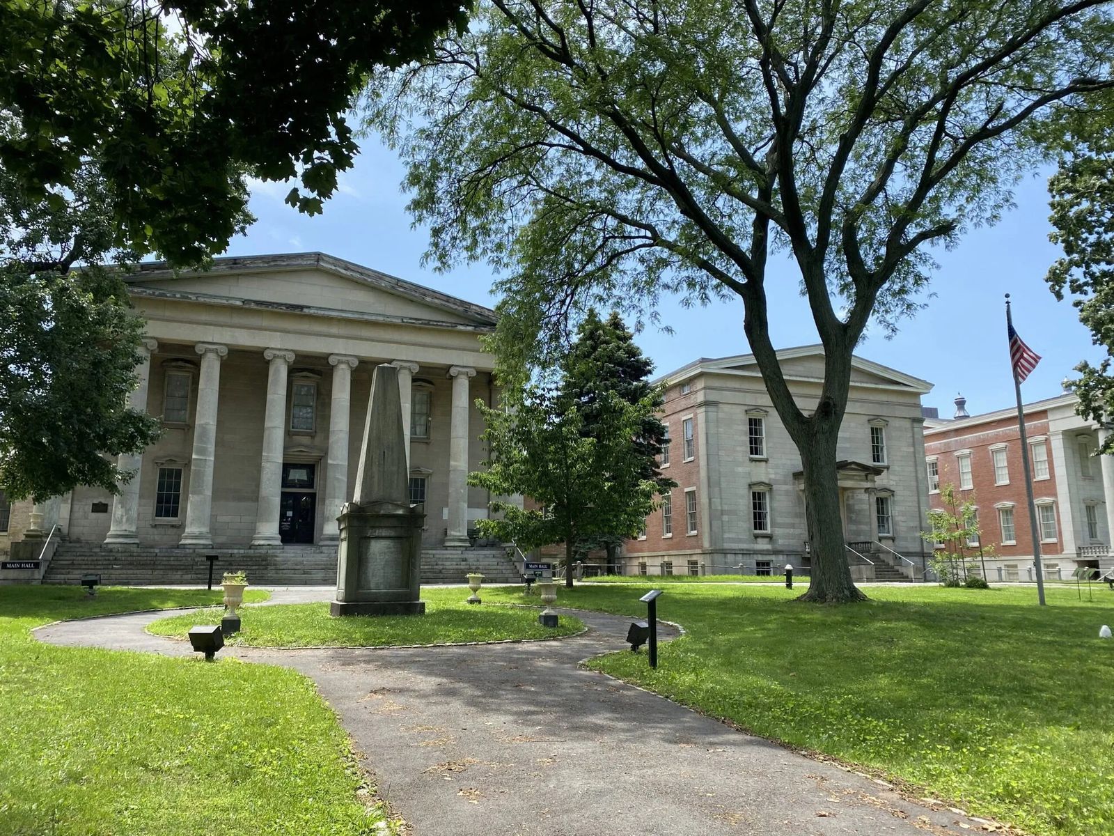 A columned historic building across a lawn with large trees and a path
