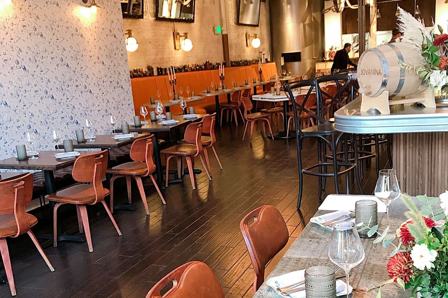 A bright dining room with orange chairs and tables set along a wall of speckled wallpaper and a bar.