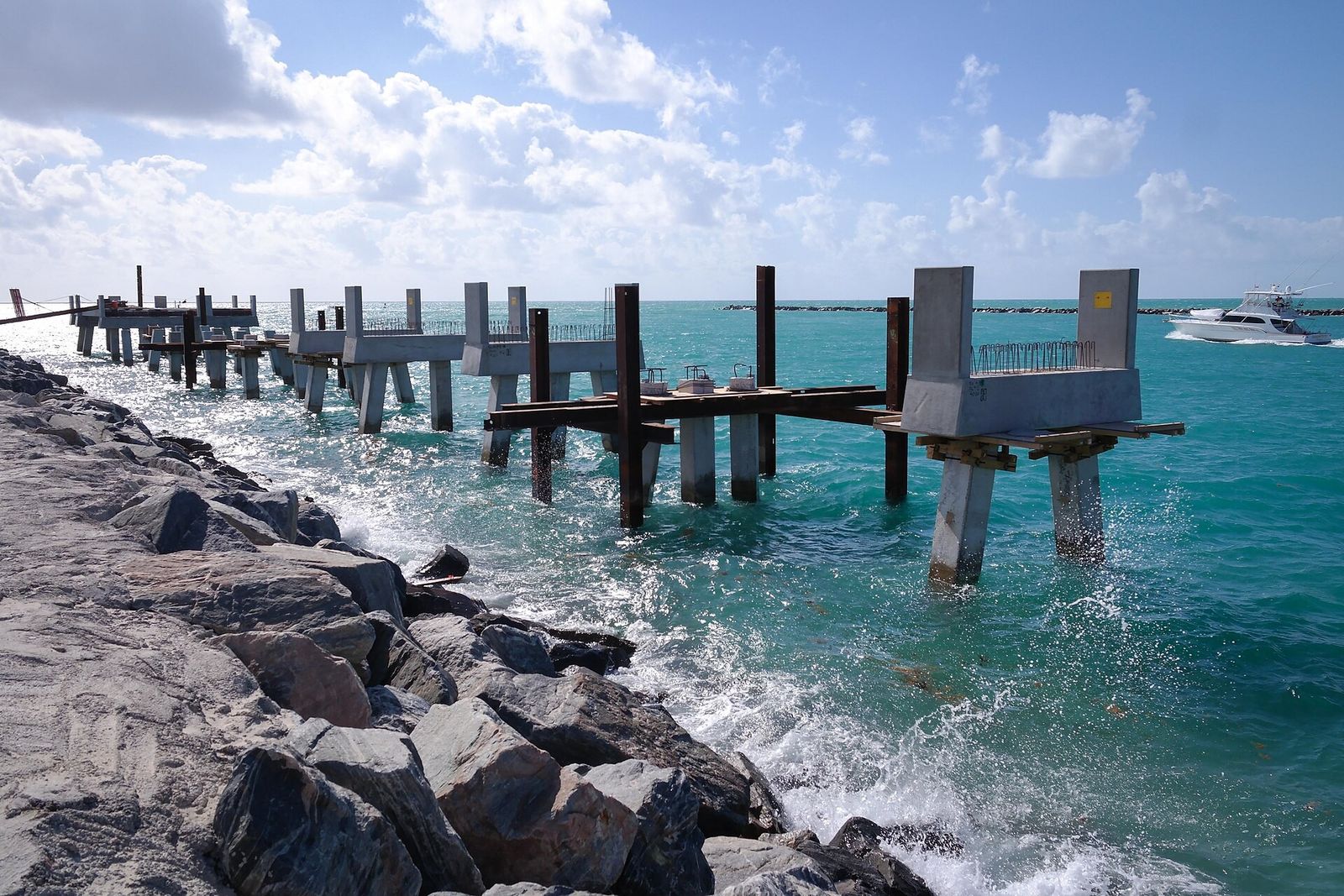 Wooden pier posts extending over turquoise water beside a rocky jetty