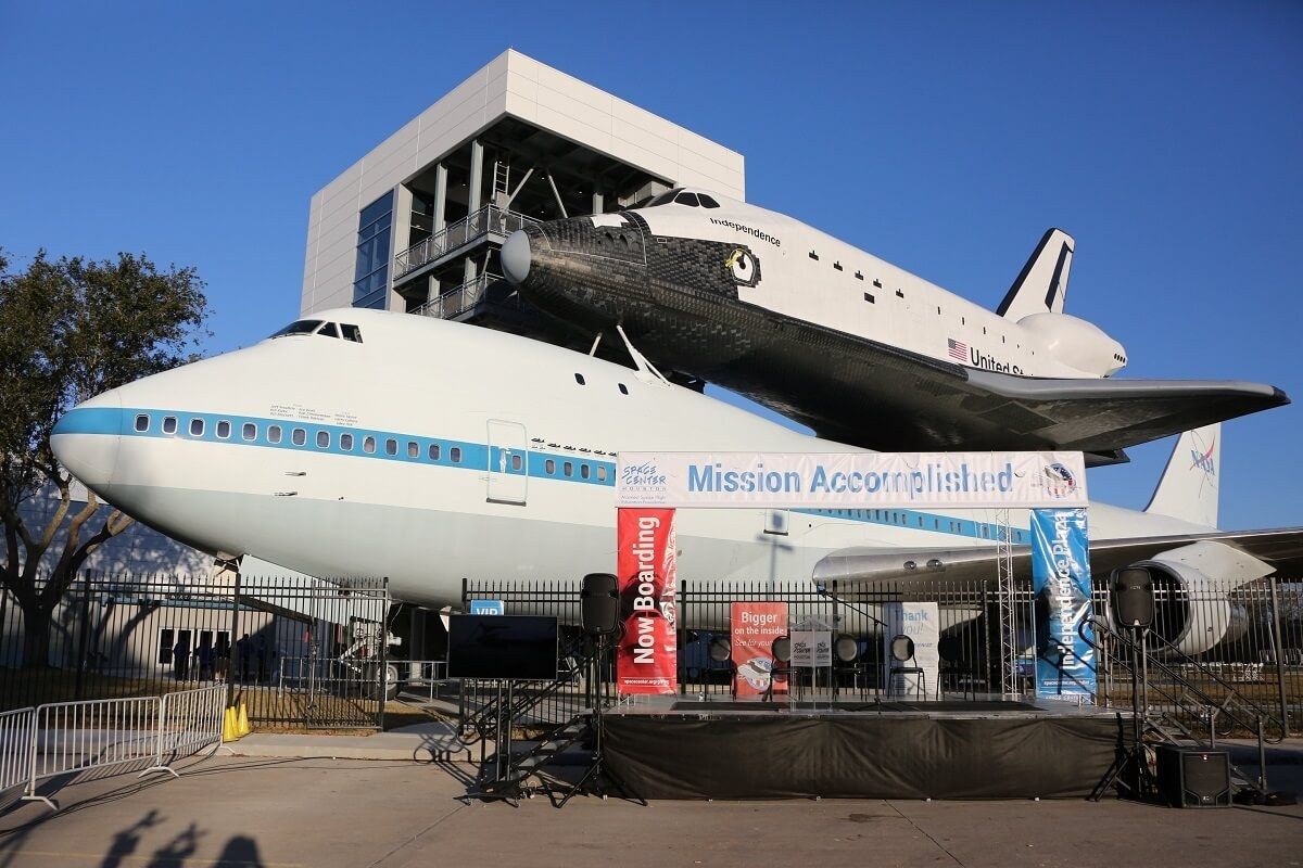 A space shuttle replica mounted on top of a jumbo jet outdoors under a blue sky