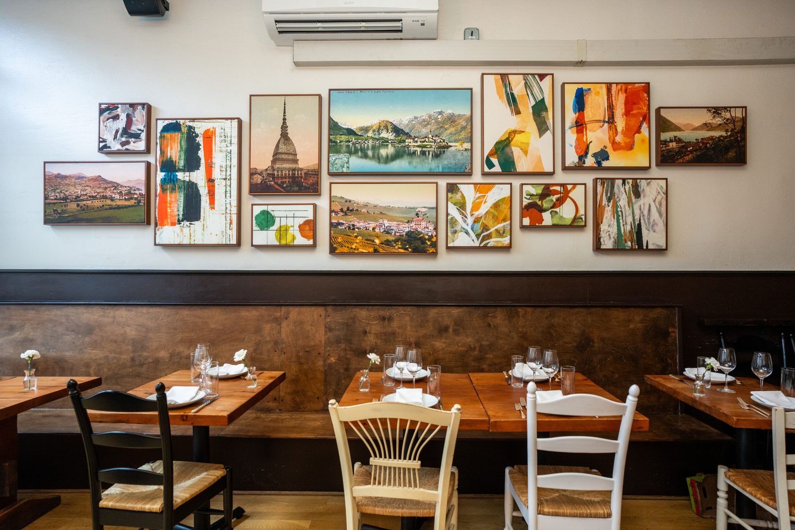A dining room with wooden tables, wicker chairs and a wall of framed colorful prints.