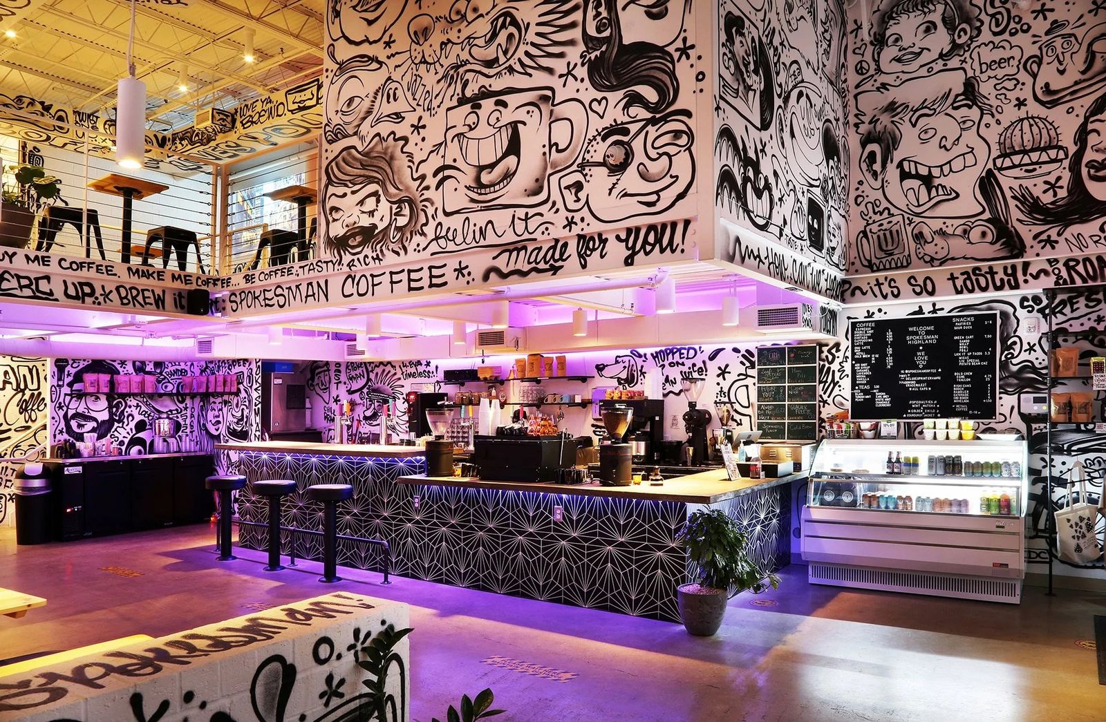 A cafe with a lit counter in purple light and walls and ceiling covered in black-and-white illustrations.