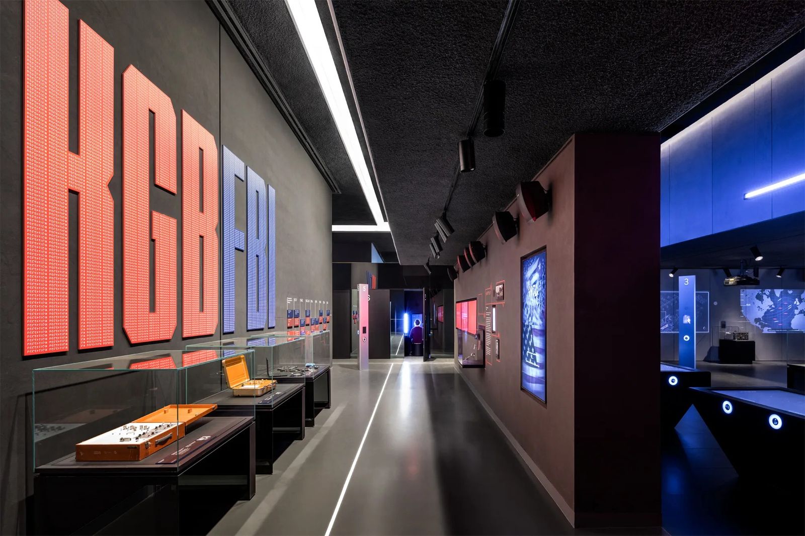 Dark museum corridor with large red block lettering on the left wall and glass display cases lit along the right