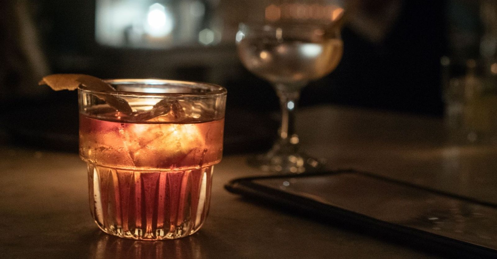 A cocktail on ice in a short glass on a dark table