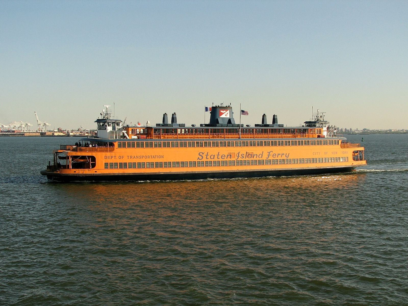 An orange Staten Island Ferry boat crossing the water at dusk