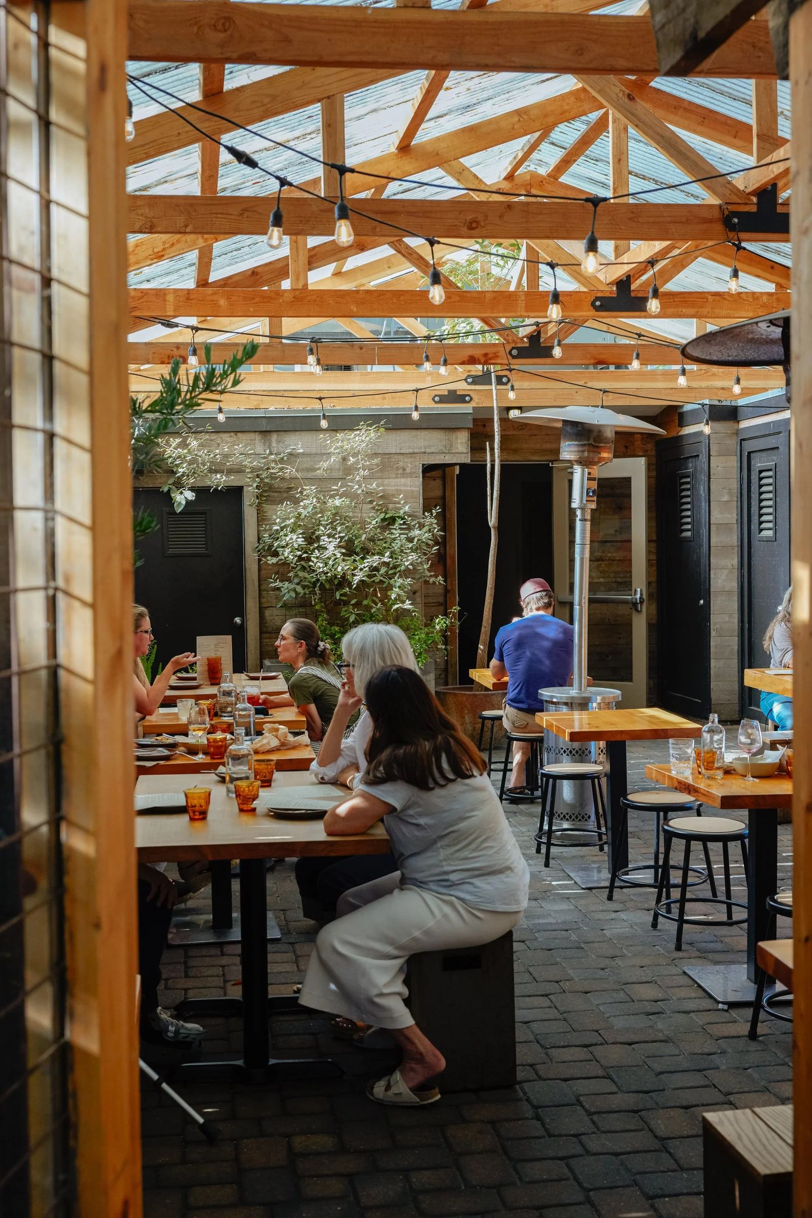 Covered patio with wooden beams and tables where a few guests sit