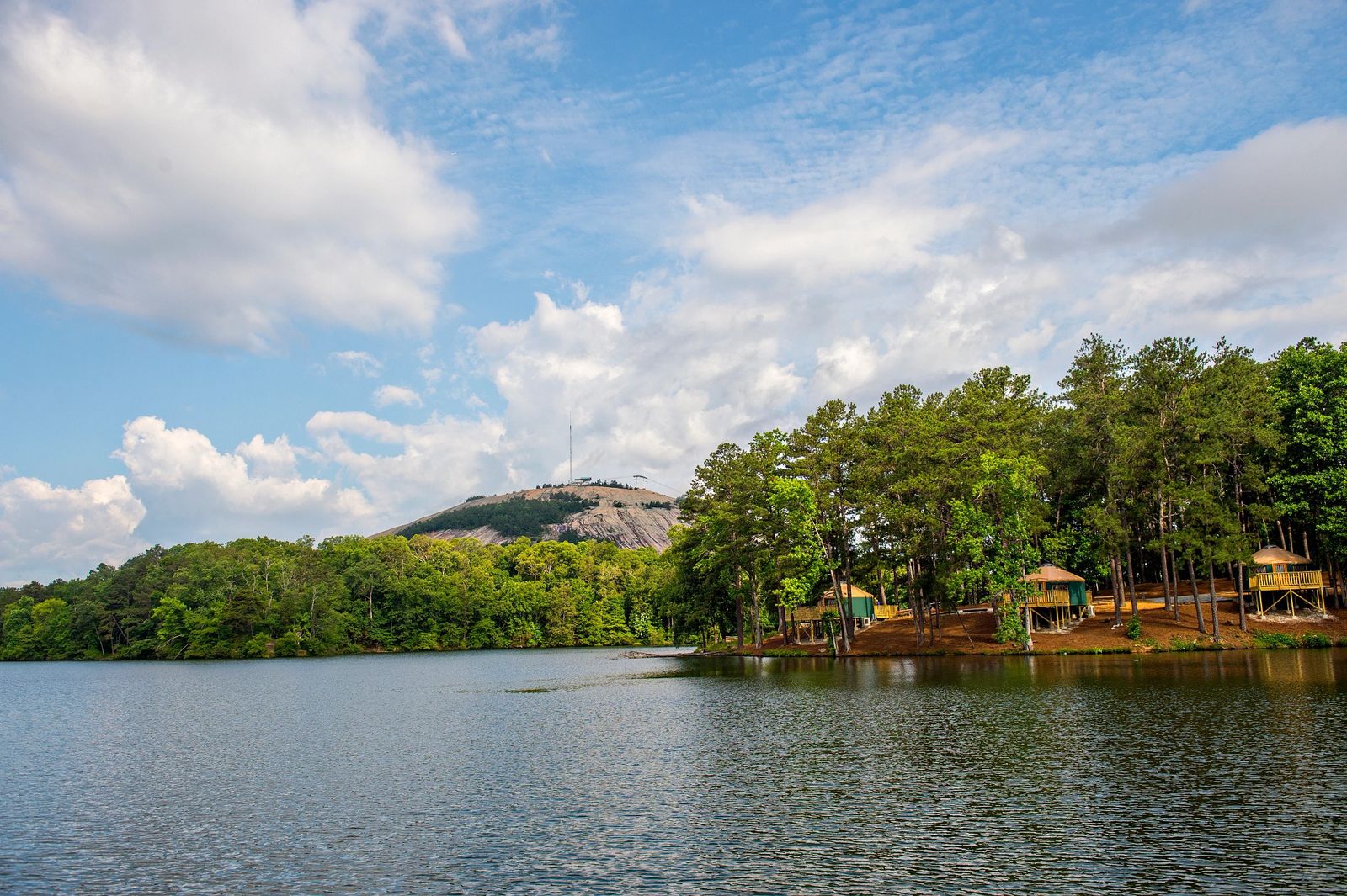 A calm lake lined with trees and small cabins, with Stone Mountain rising in the distance under a blue sky