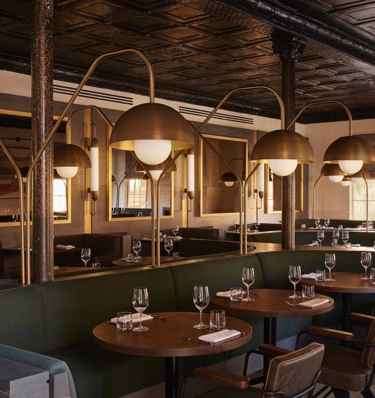 Sula dining room with green booths, round wood tables and brass dome lamps