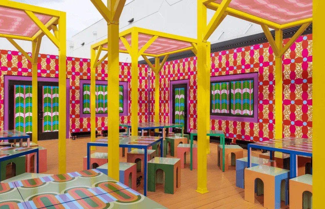 A bright event space with yellow posts, patterned walls and colorful tables and stools
