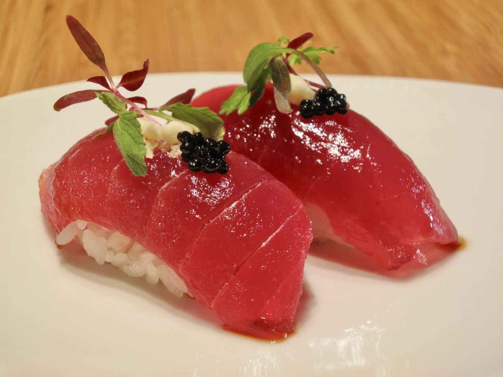 Two pieces of tuna nigiri topped with caviar and microgreens on a white plate.