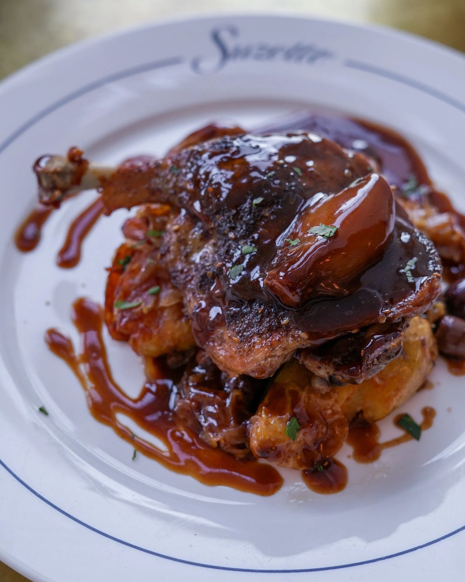 Braised meat dish in dark sauce on a white plate with blue rim and script lettering