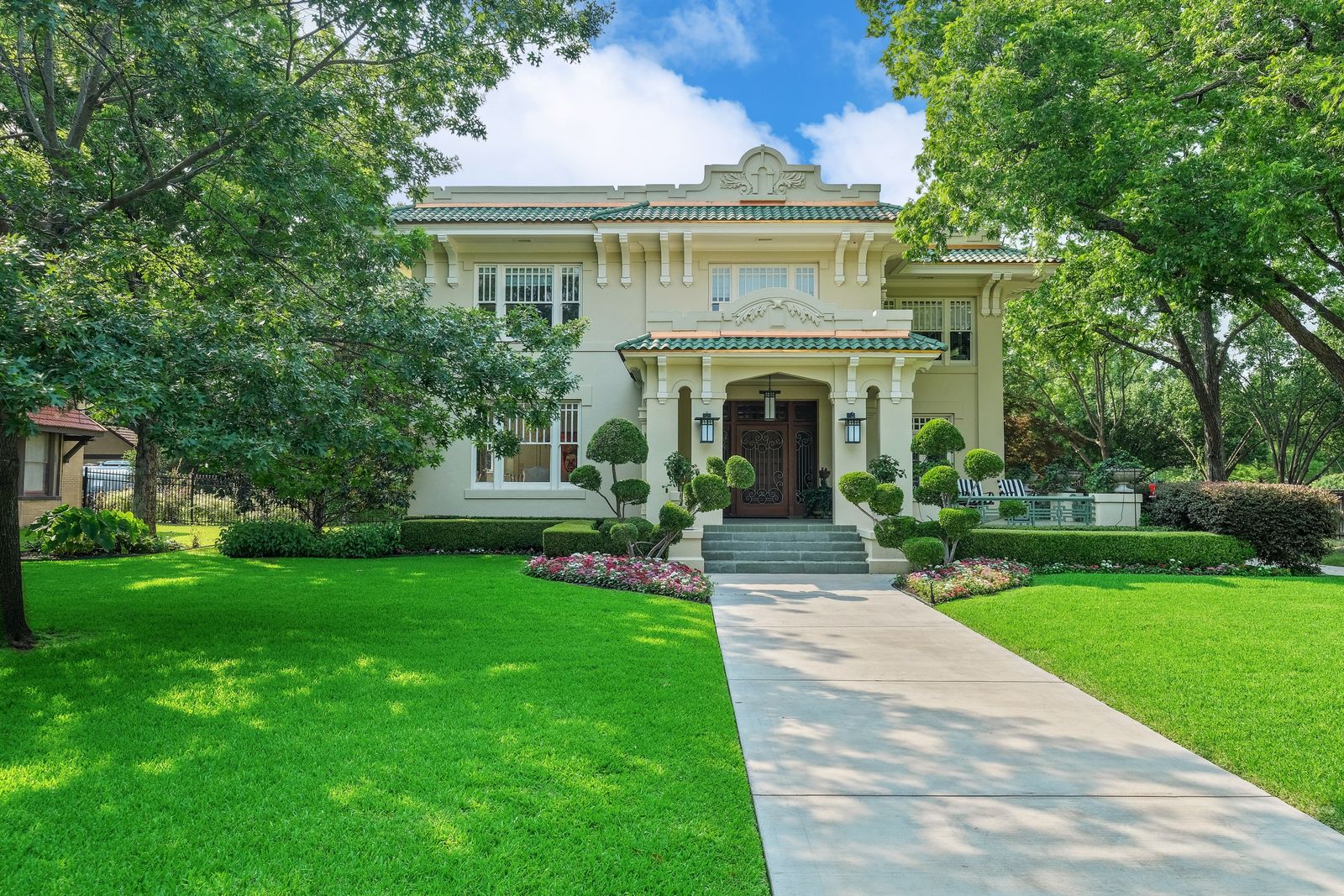 A large historic house with a columned entry and a walkway across a green lawn under mature trees.