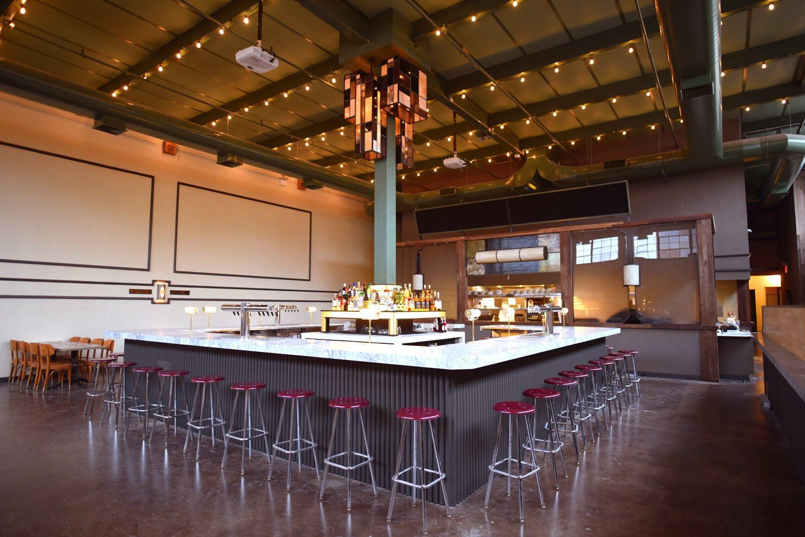 A large bar with red stools in a high-ceilinged room with string lights