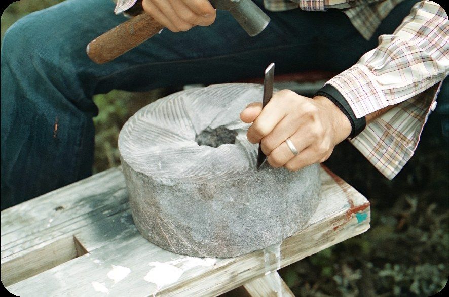 Hands striking a chisel into a round stone grinding wheel