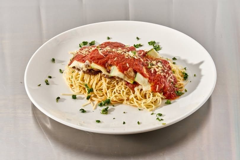 A plate of spaghetti with chicken parmesan, red sauce and parsley on a white plate.