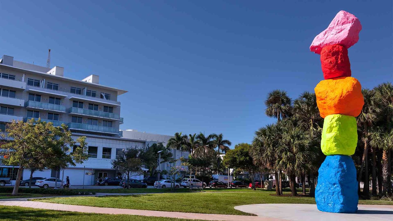 Colorful stacked-stone sculpture on a lawn beside palm trees and a white building
