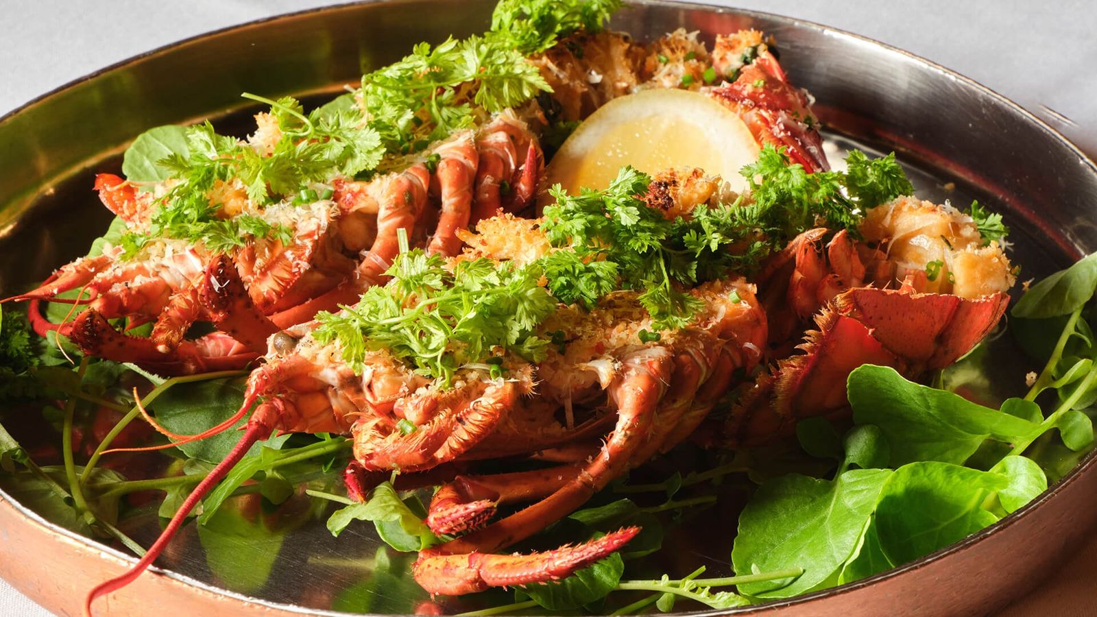 A pan of roasted lobster with greens and lemon on a copper dish.