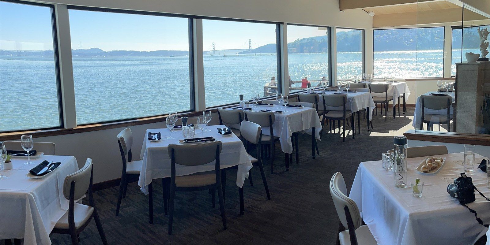 Dining room with white-clothed tables beside large windows overlooking the bay